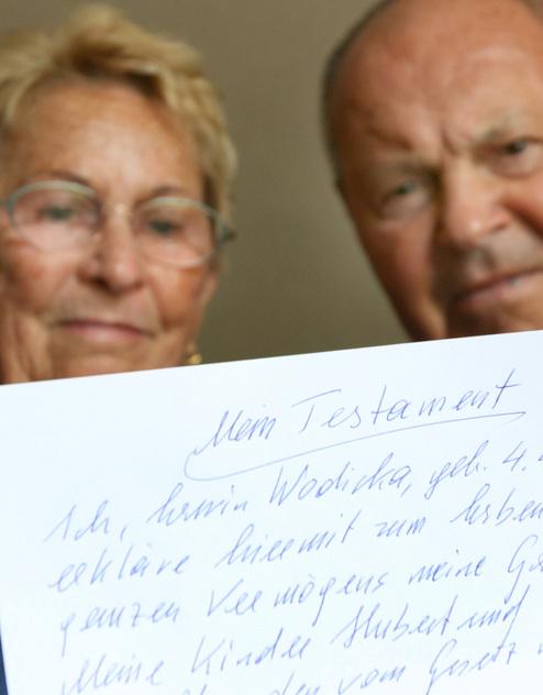 Nahaufnahme eines älteren Paares, das ein handgeschriebenes Testament auf Papier hält.